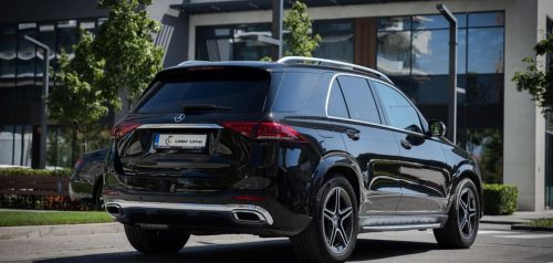 Mercedes GLE SUV vozilo limo servisa parkiran ispred zgrade, sa visokim stablima u pozadini